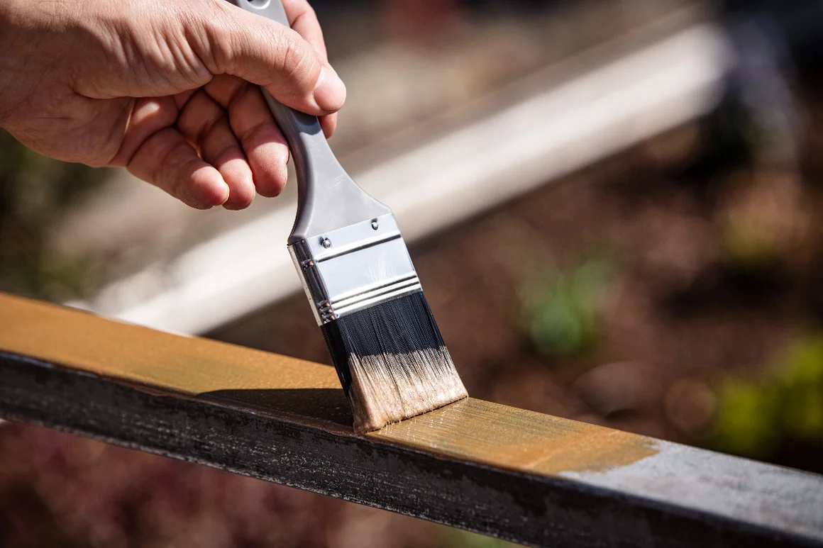 Hand streicht Metallstange mit Pinsel